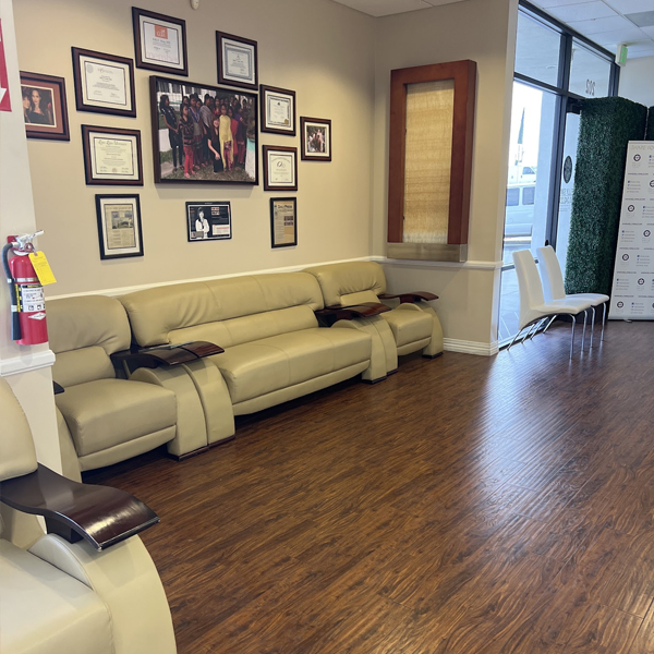 Dental office waiting room with yellow sectional sofa, framed photos on wall, and wooden flooring.