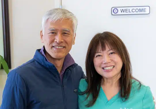 Two dental professionals smiling at camera in front of welcome sign at Kelly Smile Dentistry office.