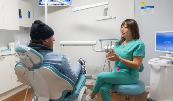 Dentist in green scrubs consulting with patient in dental chair at Kelly Smile Dentistry Victorville.