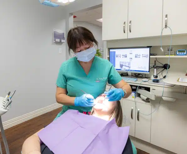 Dental hygienist in turquoise scrubs and mask performing dental treatment on patient in modern dental office.