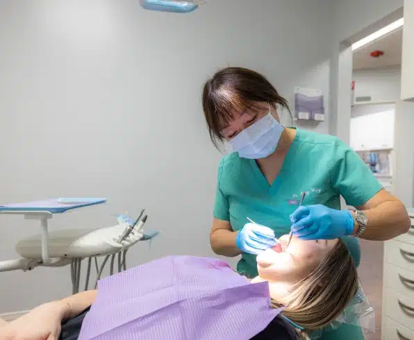 Dentist in teal scrubs and mask examines patient in dental chair at Kelly Smile Dentistry.