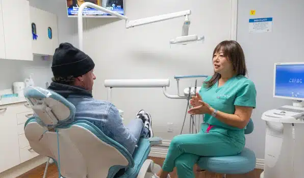 Dental hygienist in green scrubs speaking with patient in treatment chair in modern dental office.