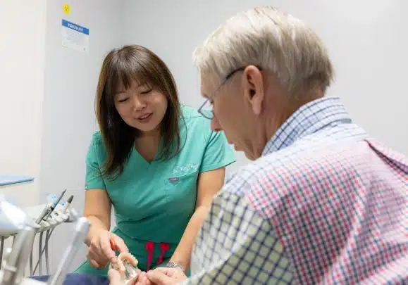 Dentist in green scrubs examining patient's teeth in clinical dental office setting.