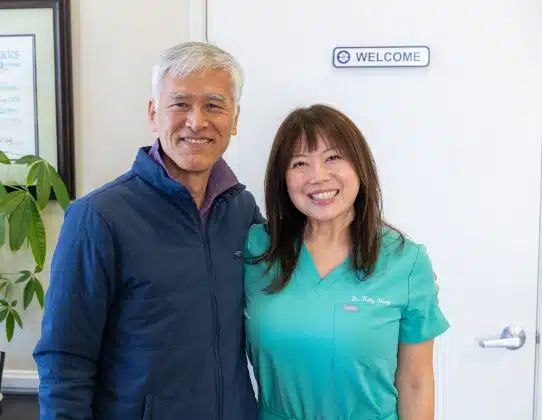 Two healthcare professionals smiling at dental office reception area with welcome sign.