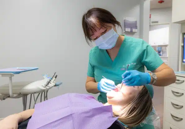 Dental hygienist in green scrubs and mask examines patient in treatment chair at Kelly Smile Dentistry.
