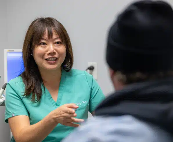 Dental professional in teal scrubs consulting with patient in modern clinic setting.