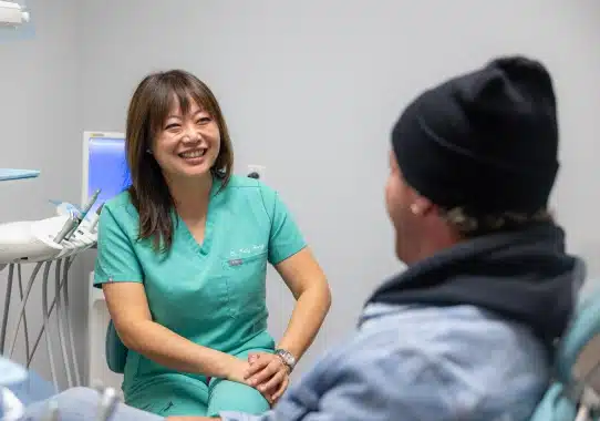 Dental professional in green scrubs smiling while consulting with patient in clinical office setting.
