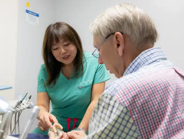 Dental hygienist in green scrubs examining patient's teeth in clinical office setting.