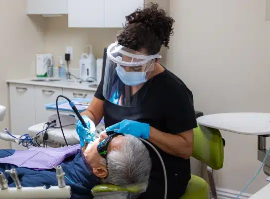 Dental hygienist examining elderly patient's teeth in modern dental office setting.