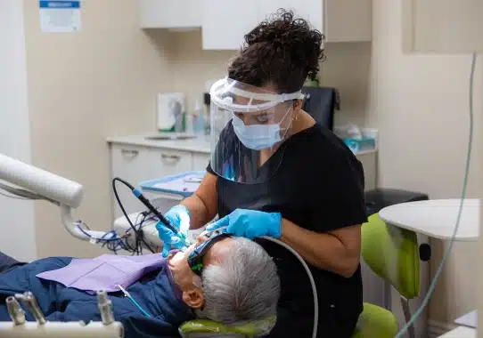 Dentist in mask and gloves performing dental examination on patient in clinical treatment room.
