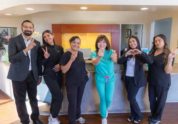 Kelly Smile Dentistry team members posing together in modern office hallway, smiling at camera.