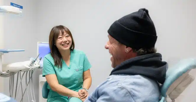 Dental hygienist in green scrubs smiling at patient in treatment room at Kelly Smile Dentistry.