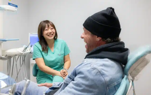 Dental hygienist in green scrubs consults with male patient in dental office treatment room.