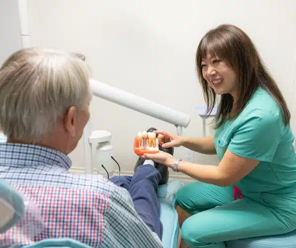 Female dental professional in green scrubs examining male patient's teeth in dental office.