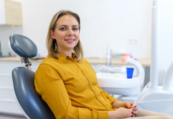 Woman in yellow shirt smiling in modern dental office treatment room.